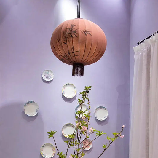 A peach-colored fabric japanese lantern painting with black bamboo leaf designs and dark fringe for dining room light