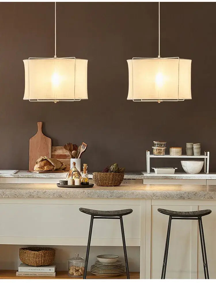 Two rectangular beige decorbites linen fabric chandelier pendant lights with thin metal frames hang above a kitchen counter