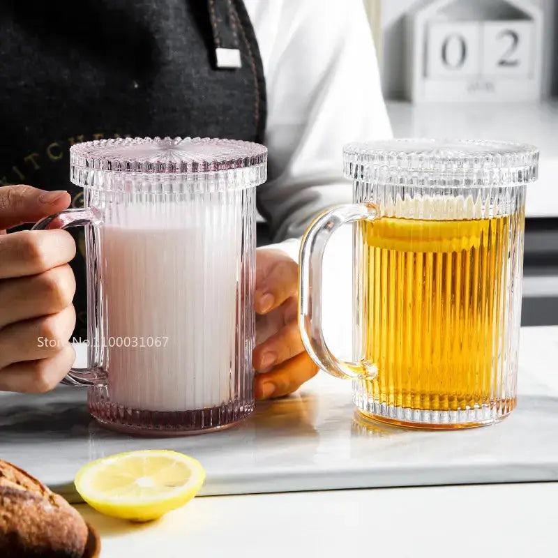 Clear glass coffee cup set with ribbed sides and lids featuring one filled with milk and one with golden beer decorbites glass coffee