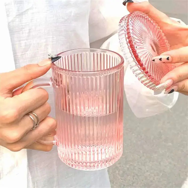 A translucent pink ribbed glass coffee cup set with lids held by hands with black nail polish for decorbites glass coffee