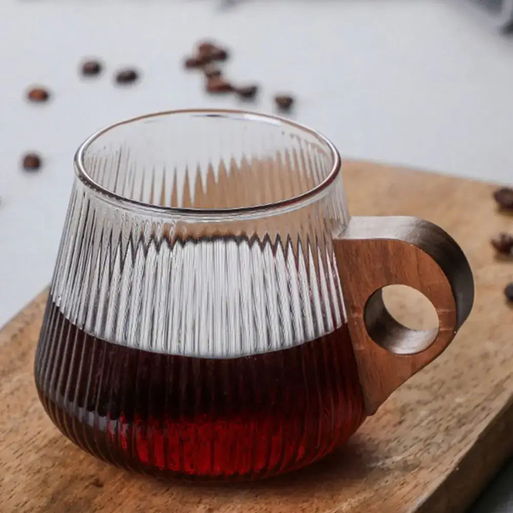 Japanese ribbed glass coffee mug with vertical texture and wooden handle filled with dark red liquid beverage