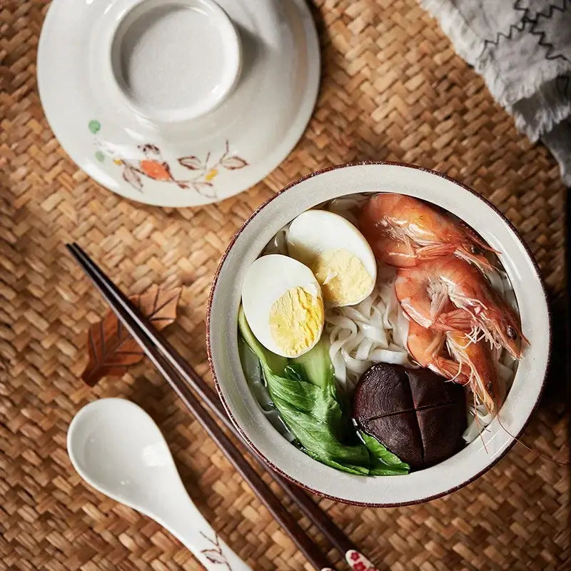 A japanese style ceramic ramen bowl with blue fish design and brown rim filled with noodles shrimp and eggs decorbites japanese style