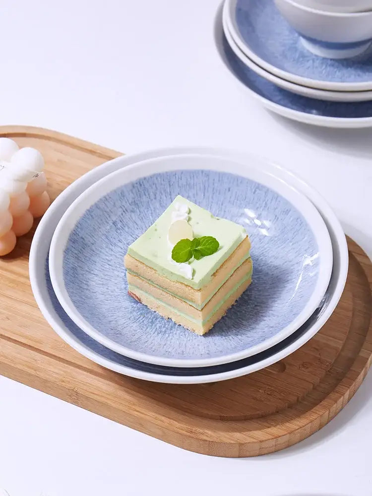 A square slice of layered green and beige cake with mint leaf on a patterned blue and white ceramic deep dish bowl
