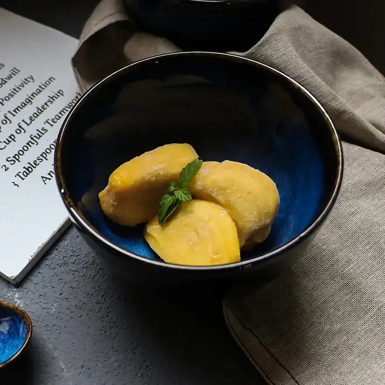 Glossy black ceramic salad bowl with vibrant blue interior holding mango slices and mint leaves from decorbites ceramic salad set