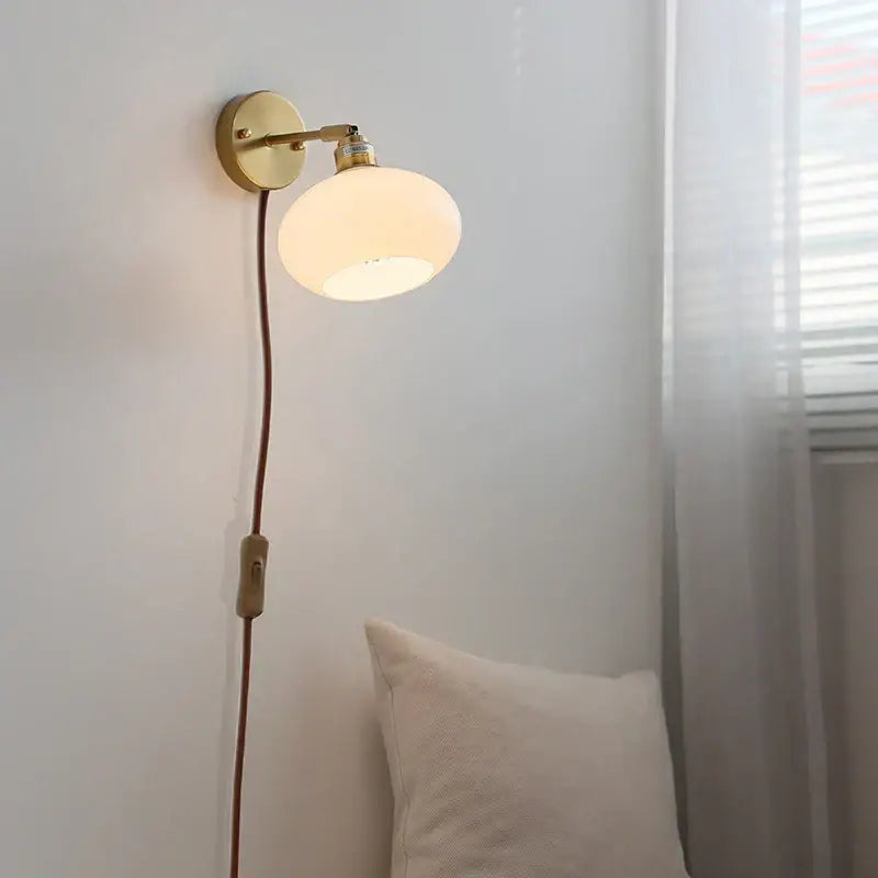 A warm glowing japanese style led brass wall sconce with off-white frosted glass globe and pull chain for bedroom decor