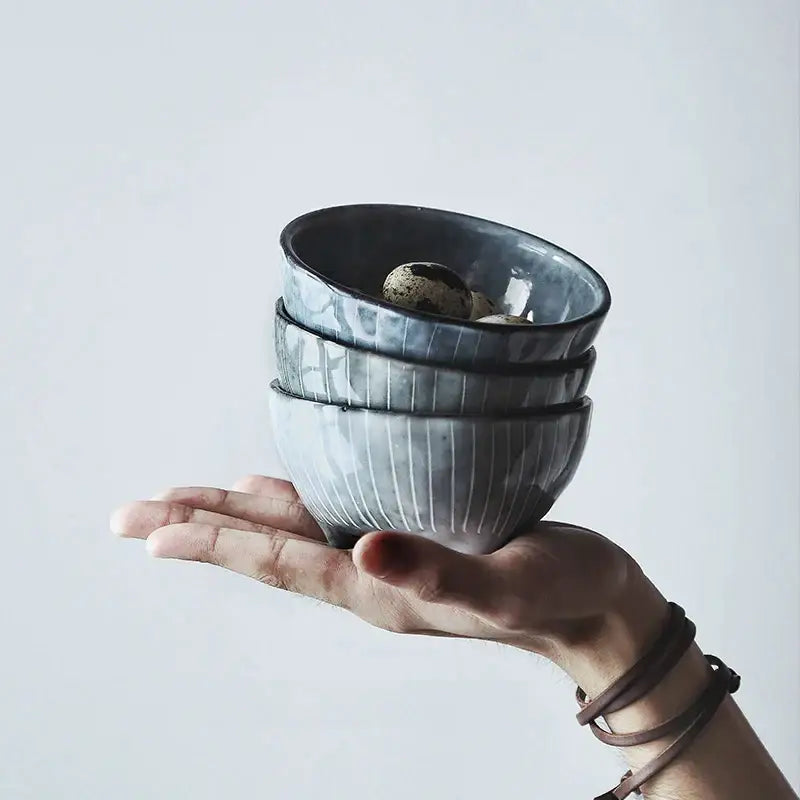 Stack of three gray ceramic small sauce dishes rice bowl with vertical ridges each holding a speckled quail egg