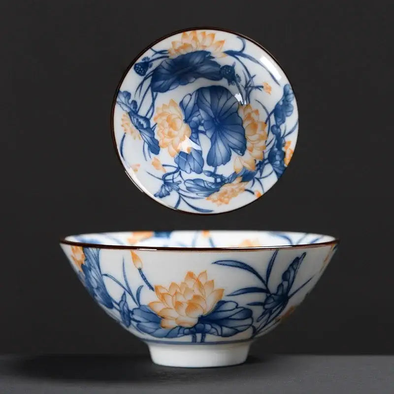 A white ceramic kung fu tea cup with intricate blue and orange lotus blossoms and a subtle brown rim decorbites blue design