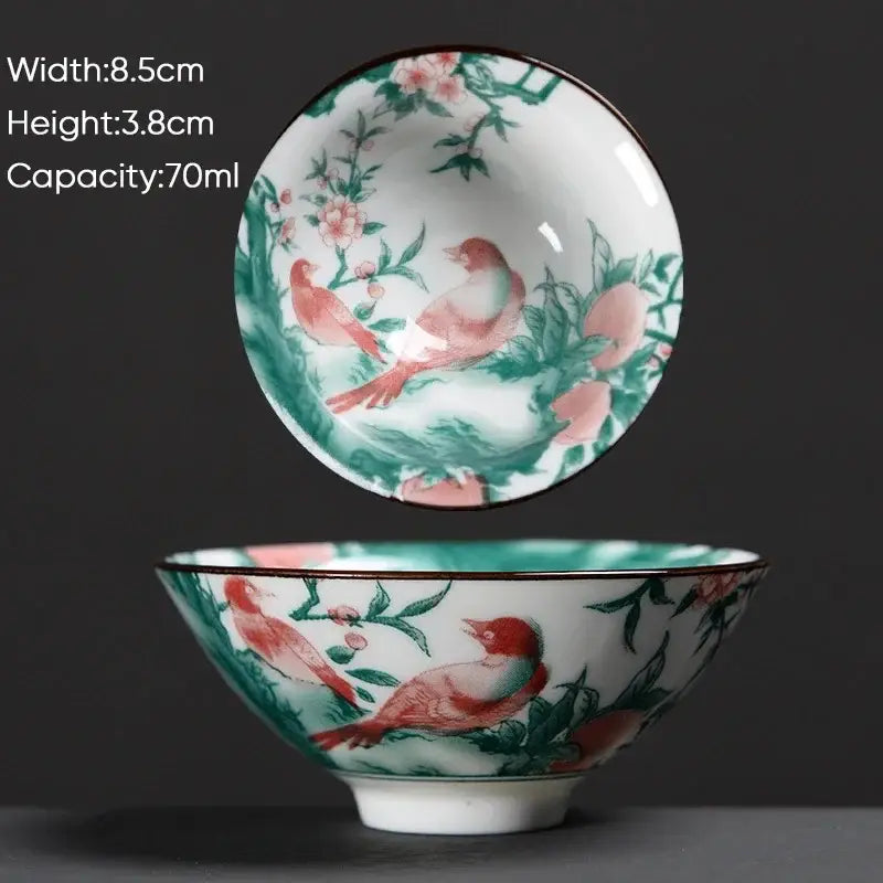 A delicate white ceramic kung fu tea cup with hand-painted pink birds green foliage and a dark rim decorbites blue style