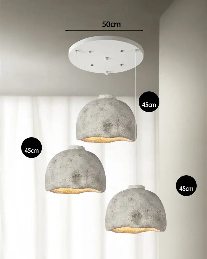 Set of three gray concrete resin pendant lights with warm interiors suspended from a white ceiling mount for dining room