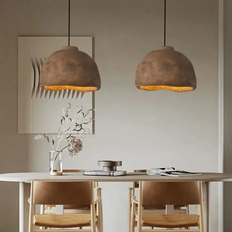 Two earthy-toned textured concrete resin pendant lights with warm amber glow for japanese style rustic dining room