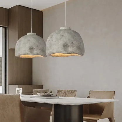 Two gray textured concrete resin pendant lights with warm golden interiors hang above a dining table