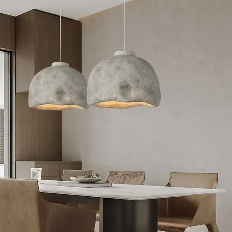 Two gray textured concrete resin pendant lights with warm golden interiors hang above a dining table