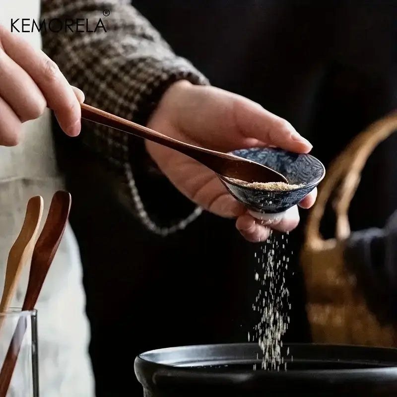Dark blue ceramic bowl with white patterns held while seasoning pot alongside japanese style wooden spoon set natural wood tools