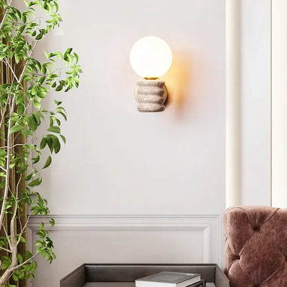 A warm spherical glass bulb led wall lamp mounted on a textured japanese travertine concrete base for bedroom use