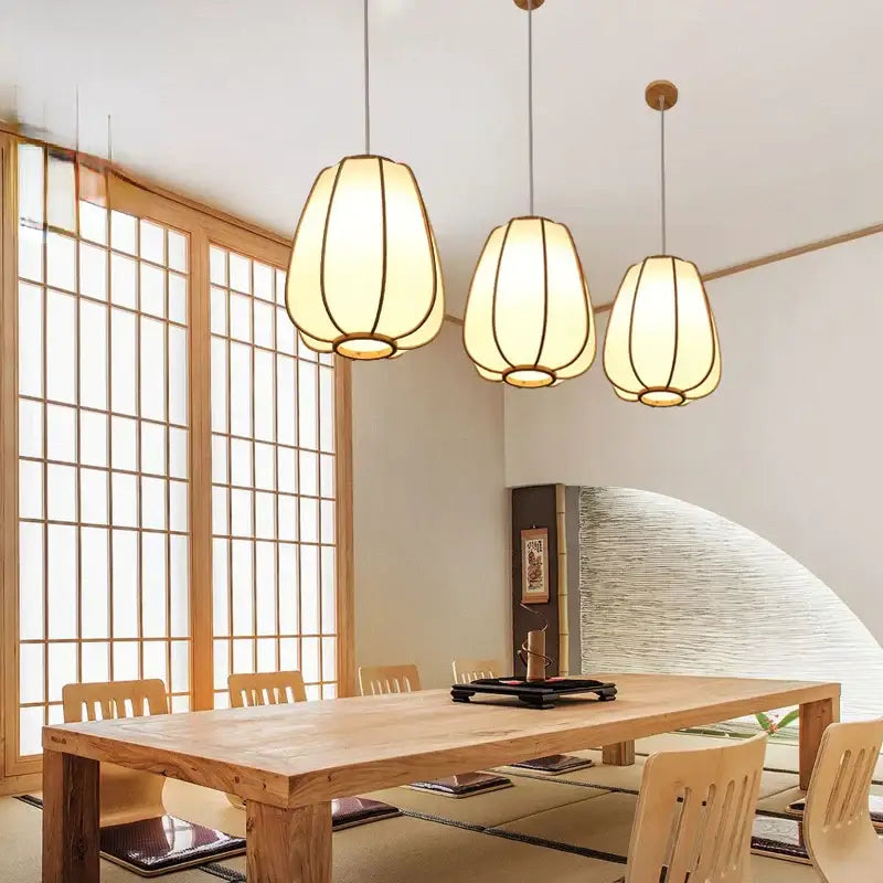 Three warm-toned bamboo pendant lamps with woven fabric shades and wooden frames above a rustic dining table decorbites bamboo pendant
