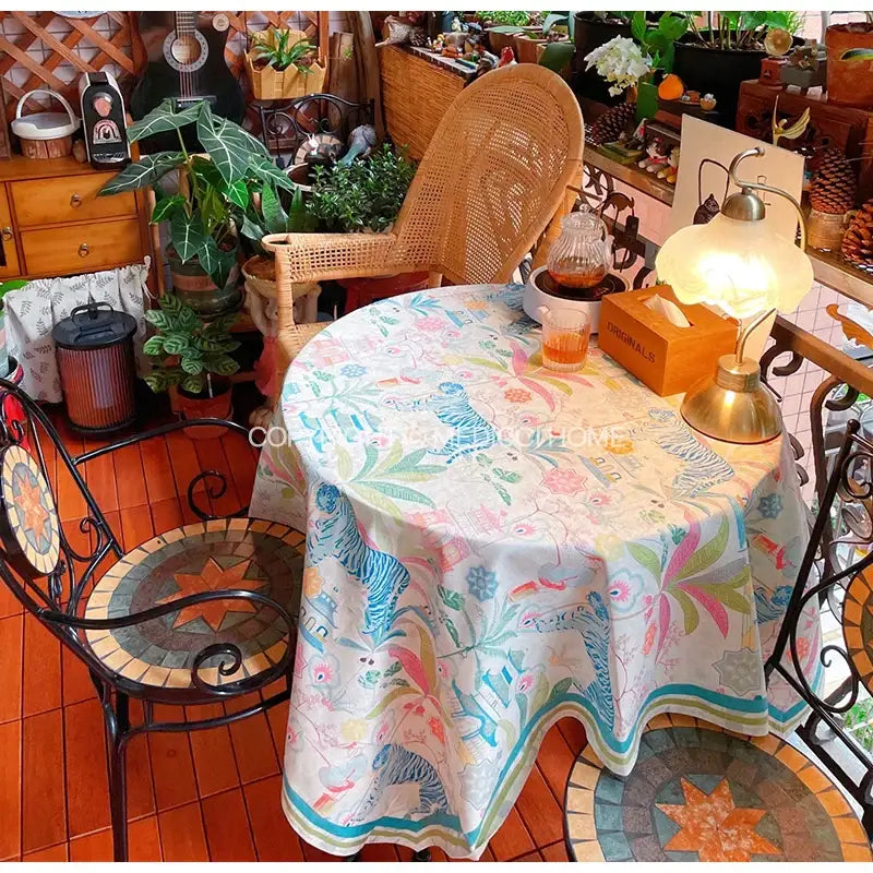 A decorbites jungle vibes tablecloth in cream blue and green with whimsical tiger print and tropical foliage decor