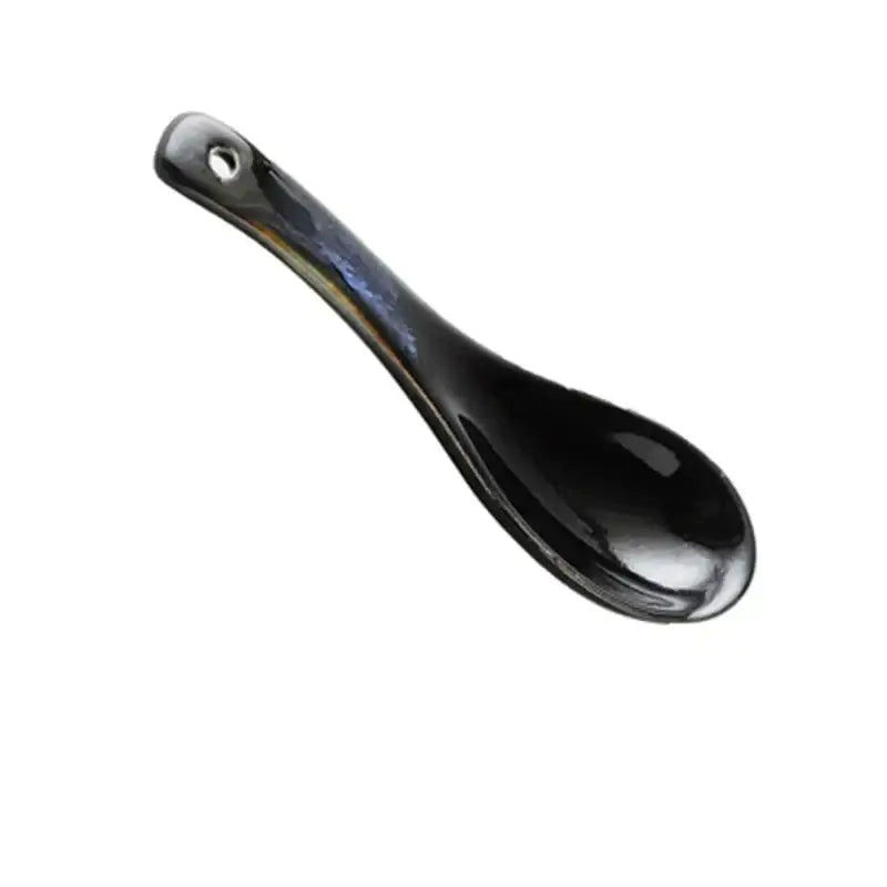 A sleek glossy black ceramic spoon with a small hole complements the kiln glazed blue speckled ramen bowl dining dish