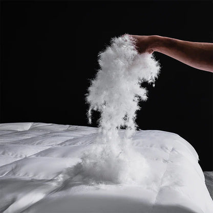 A fluffy white down filling cascading from a king size goose down and silk quilted comforter for master bedroom luxury