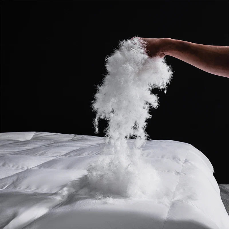 A fluffy white down filling cascading from a king size goose down and silk quilted comforter for master bedroom luxury