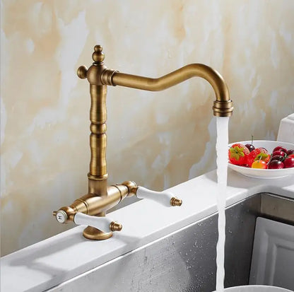 Antique brass single hole kitchen faucet with white ceramic handles and curved spout water flowing from nozzle