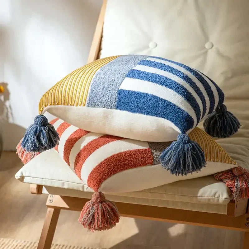 Two stacked decorbites knit stripe pillow covers in mustard yellow, blue, white, terracotta, and cream with tassels