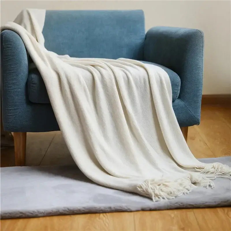 Cream-colored soft textured decorbites knitted cashmere siesta blanket with fringed edges draped on blue armchair