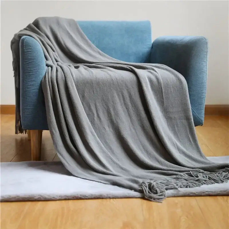 A soft medium-gray decorbites knitted cashmere siesta blanket with textured weave and fringed edges draped over a blue armchair