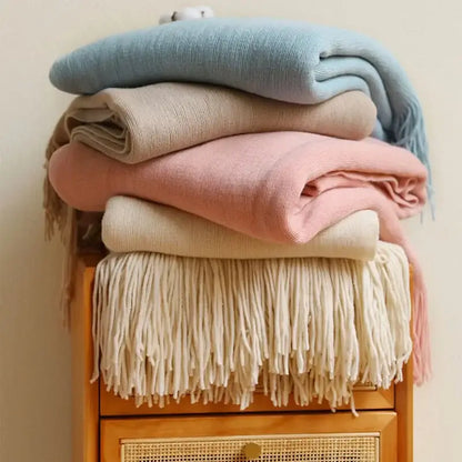 Stack of pastel-colored decorbites knitted cashmere siesta blankets with fringe detailing for bedroom decor