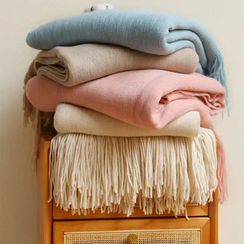 Stack of pastel-colored decorbites knitted cashmere siesta blankets with fringe detailing for bedroom decor
