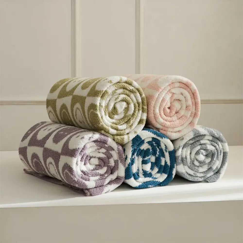 A plush knitted checkboard smile face gray and white bedroom throw blanket with olive green and white swirling pattern rolled up