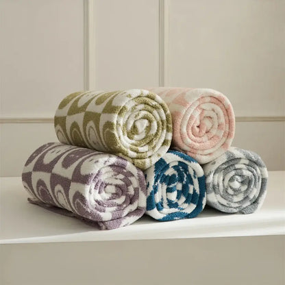 A plush knitted checkboard smile face gray and white bedroom throw blanket with olive green and white swirling pattern rolled up