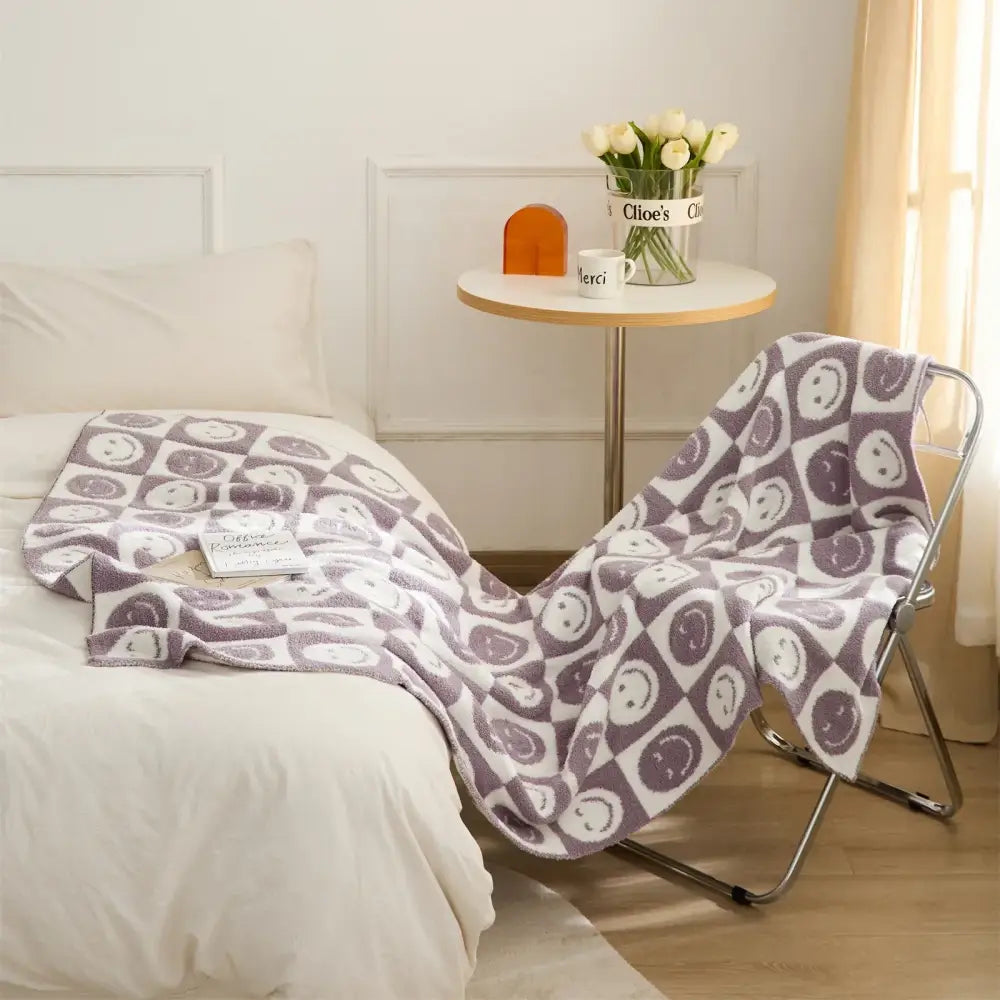 A cozy gray and white knitted checkboard smile face blanket draped over a metal chair for bedroom decorbites throw