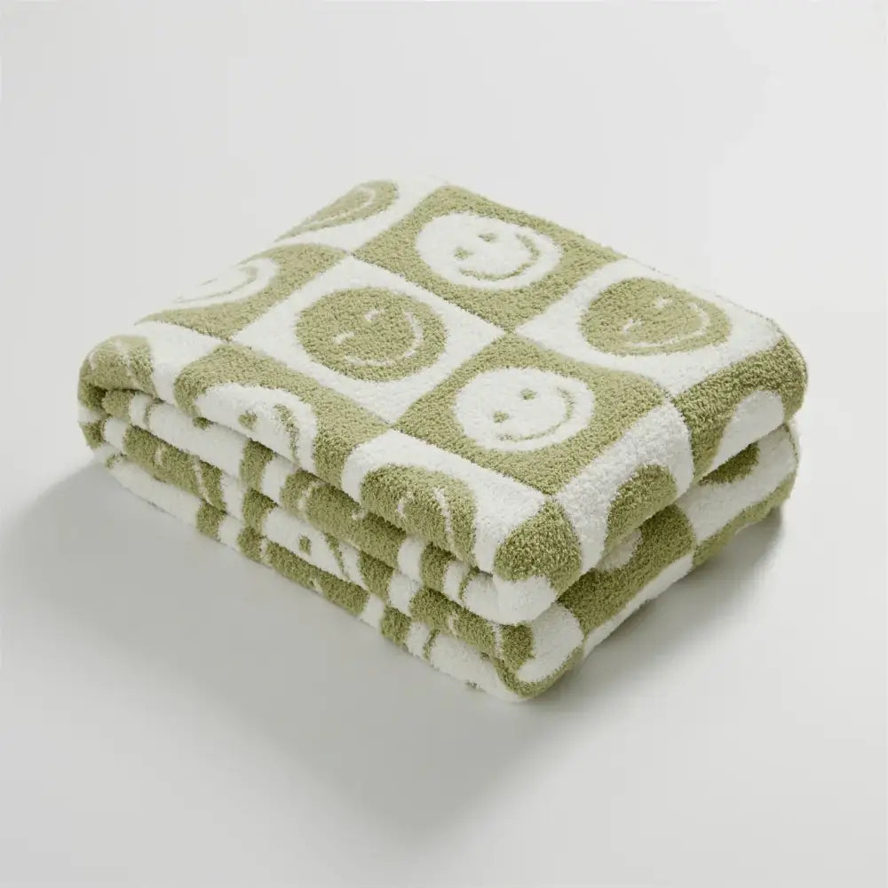 A soft knitted checkboard smile gray and white blanket folded with olive green and white checkboard smile face pattern