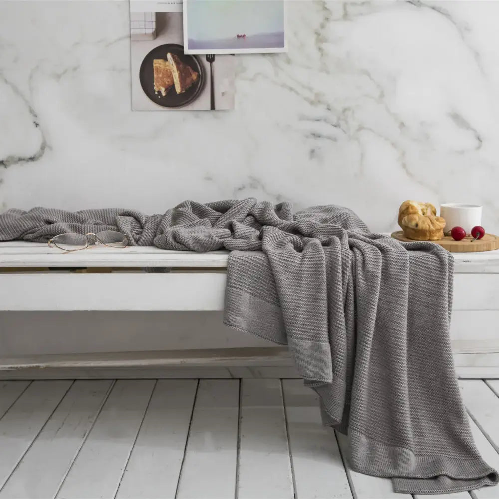 Gray knitted bamboo cooling throw blanket with textured weave and ribbed edges draped over white bench