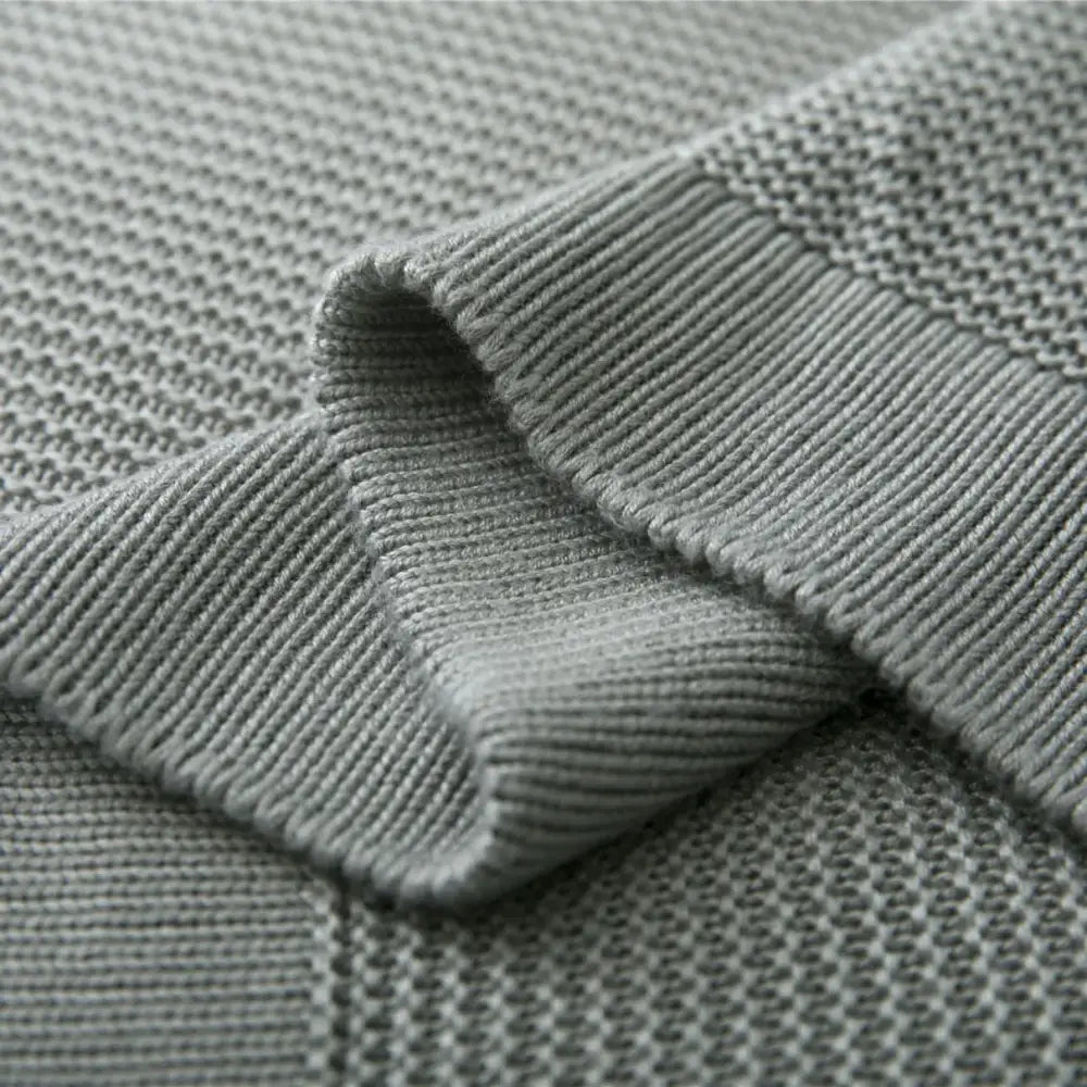 A soft heather gray knitted sweater with textured pattern and ribbed cuffs beside a light blue bamboo cooling throw blanket