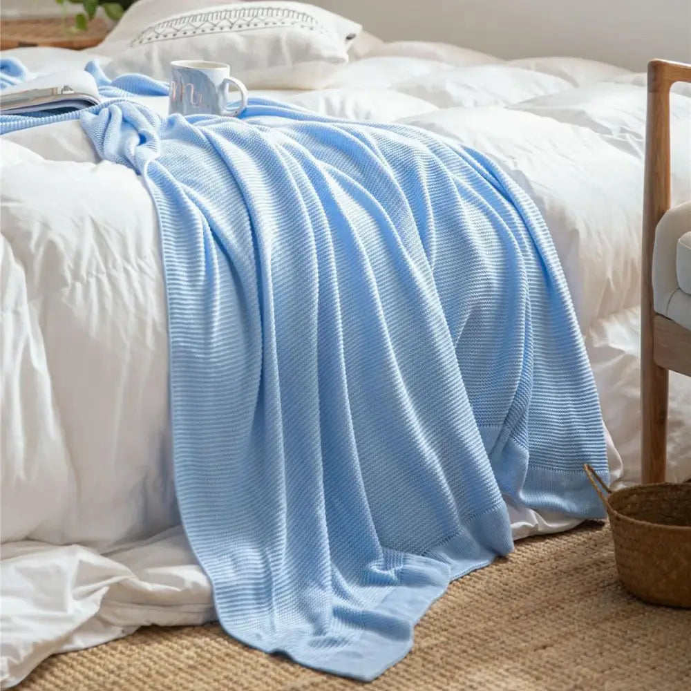 A soft light blue knitted bamboo cooling throw blanket with a textured waffle pattern draped over a bed