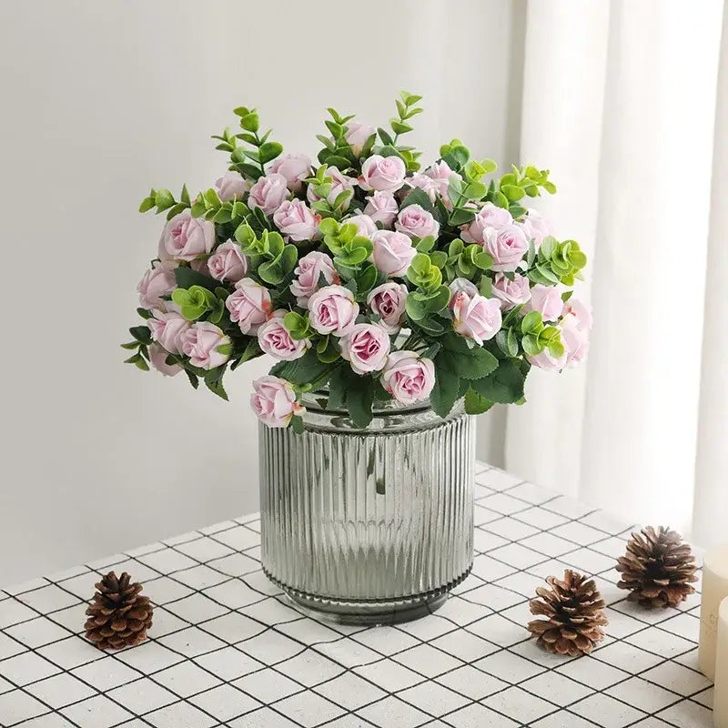 A Korean style pink and white artificial roses bouquet with lush green foliage in a clear ribbed glass vase for home decor