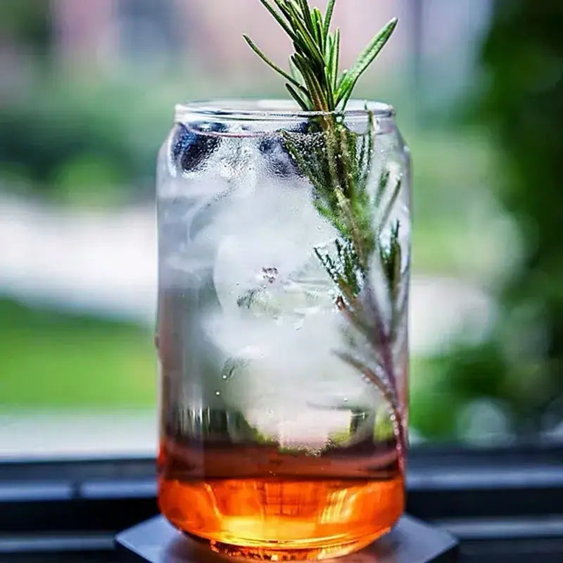 A large can shape beer glass cup with metal straw containing amber liquid, ice, blueberries, and rosemary garnish