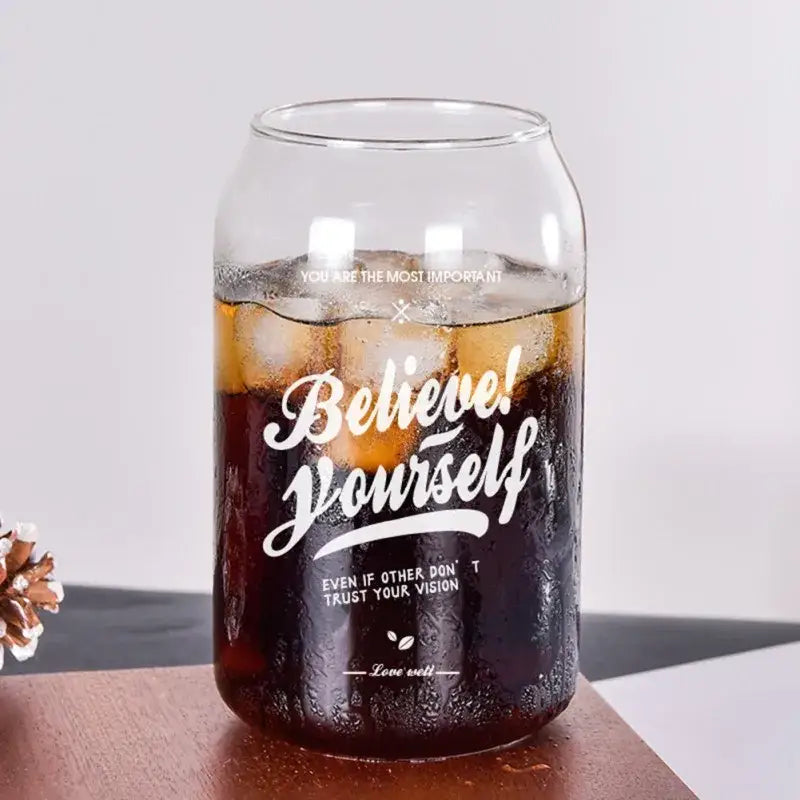 Clear glass can shape beer glass cup with white engraved motivational text filled with iced dark soda and metal straw