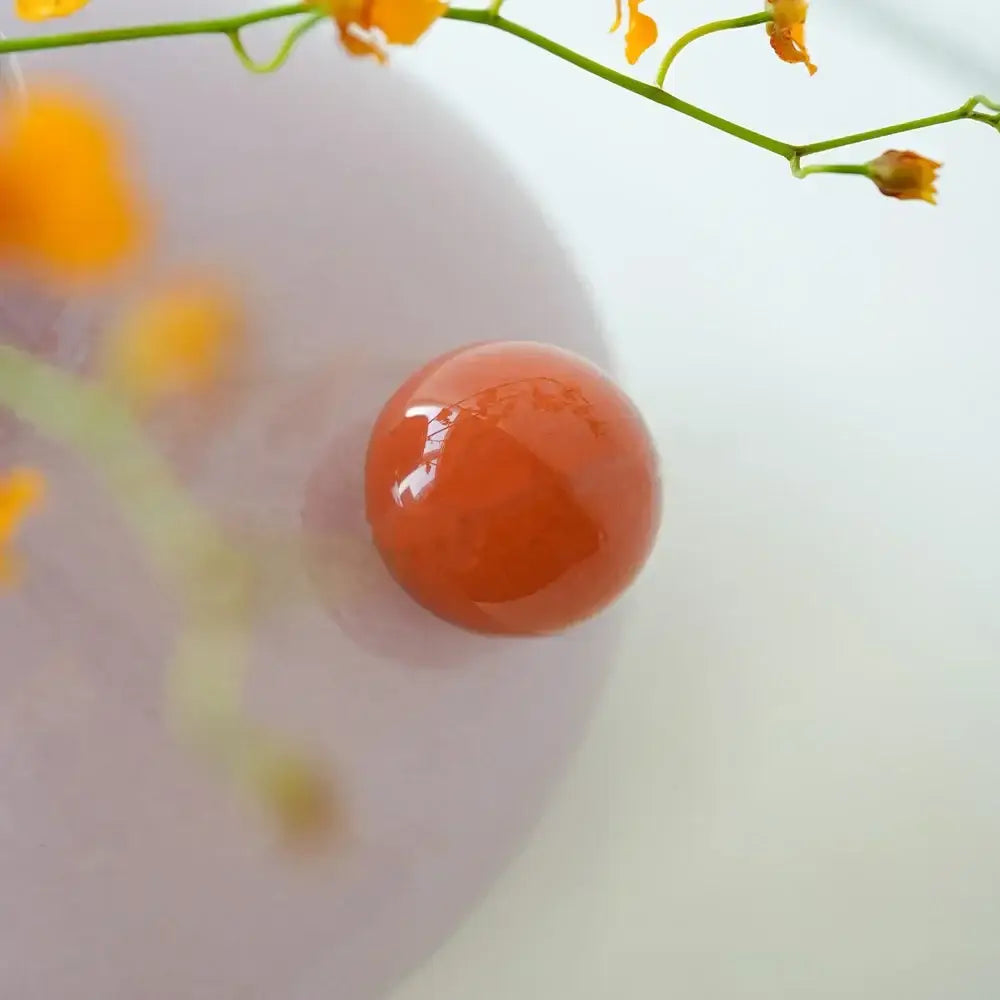 A smooth translucent orange gemstone with polished surface beside decorbites geometric glass vase in lavender and blush pink