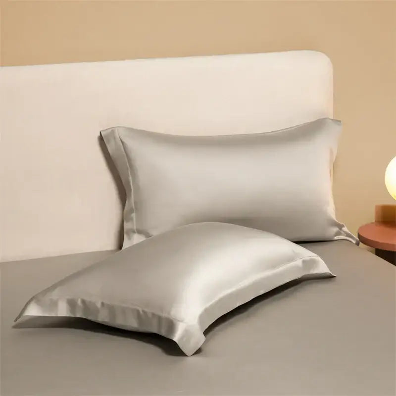 Two elegant silver satin egyptian cotton pillowcases in a cotton pillowcase set resting on a bed