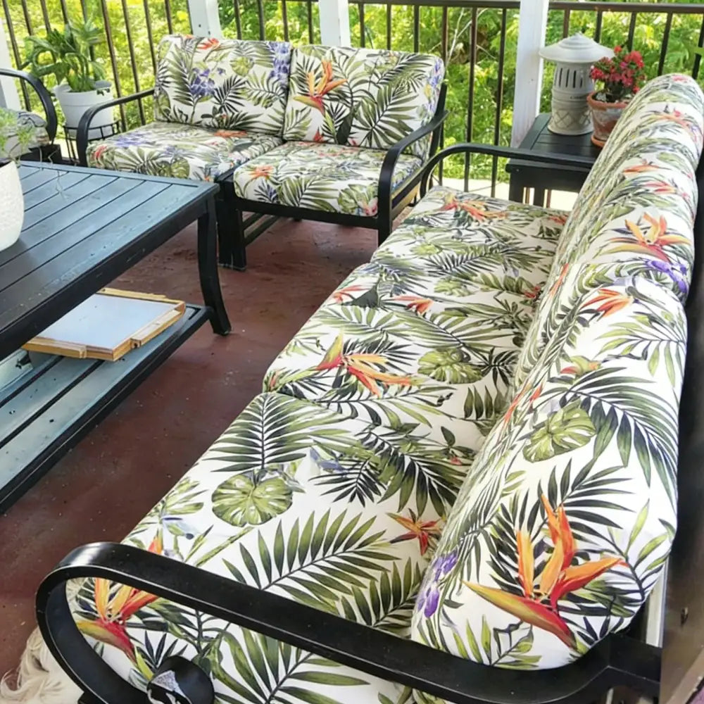Black metal-framed outdoor sofa with brushed knit tropical leaf and bird-of-paradise cushion cover in vibrant colors