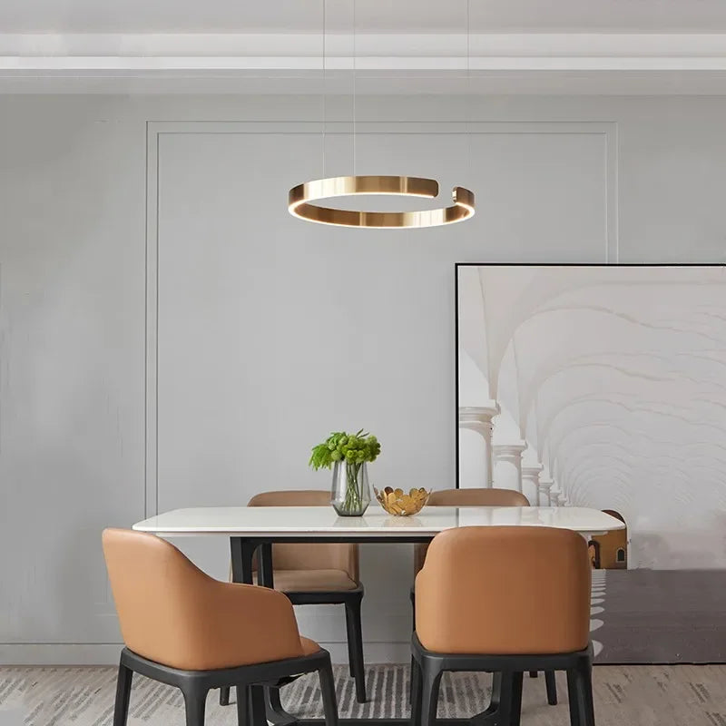 Modern gold-toned led chandelier light with circular rings design hanging above dining table for kitchen or study