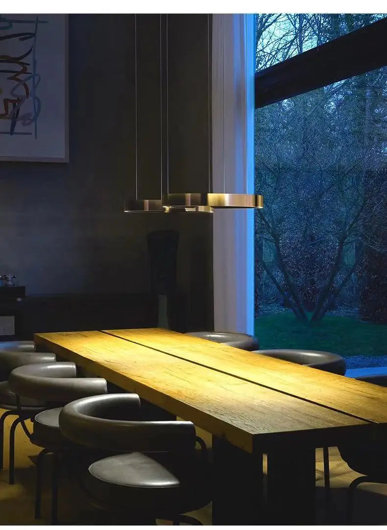 Modern brass led chandelier light with sleek cylindrical design hanging above wooden dining table for dining room