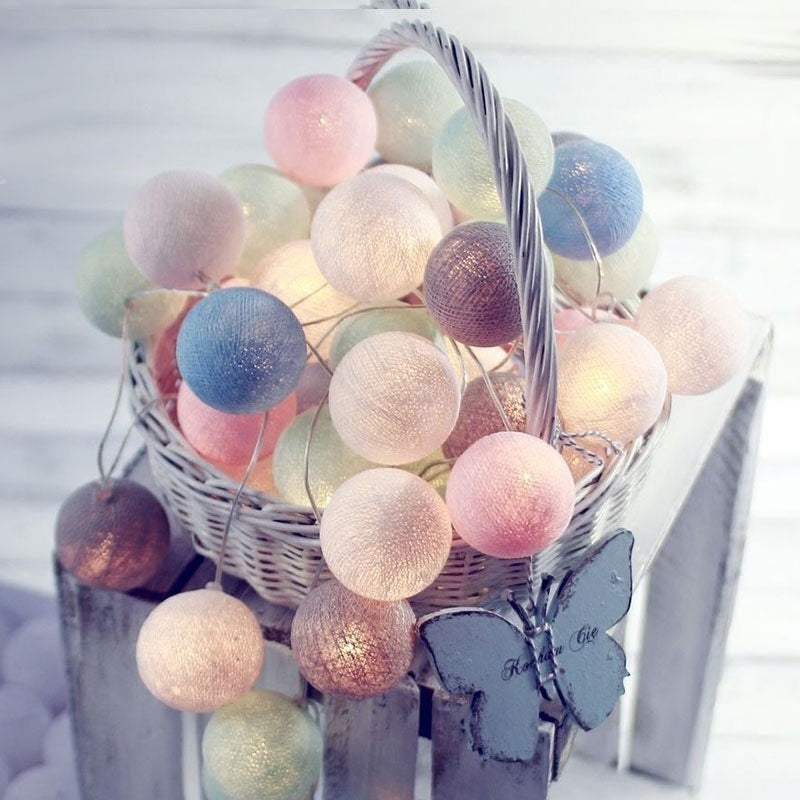 Pastel-colored cotton ball string lights with butterfly accents in a white wicker basket.