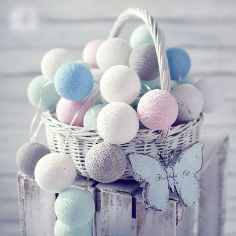 Pastel-colored cotton ball garland in a white wicker basket with wooden butterflies.