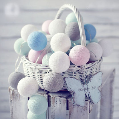 Pastel-colored cotton ball garland in a white wicker basket with wooden butterflies.