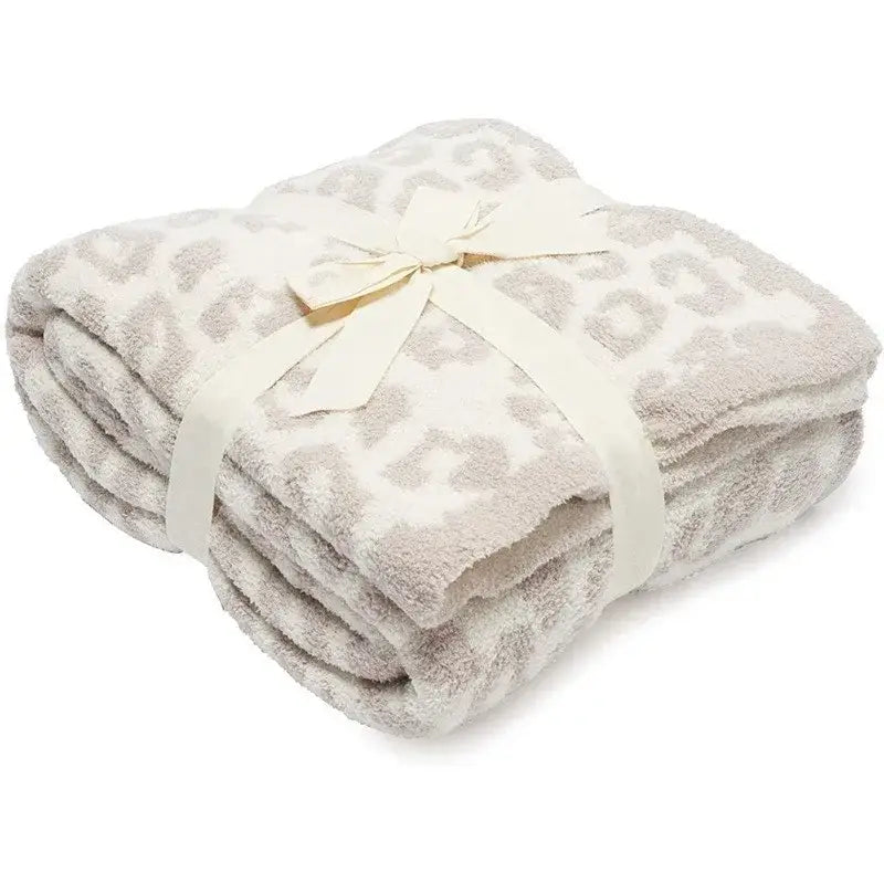 A cream-colored fleece blanket with subtle gray leopard print tied with an ivory ribbon by decorbites leopard print