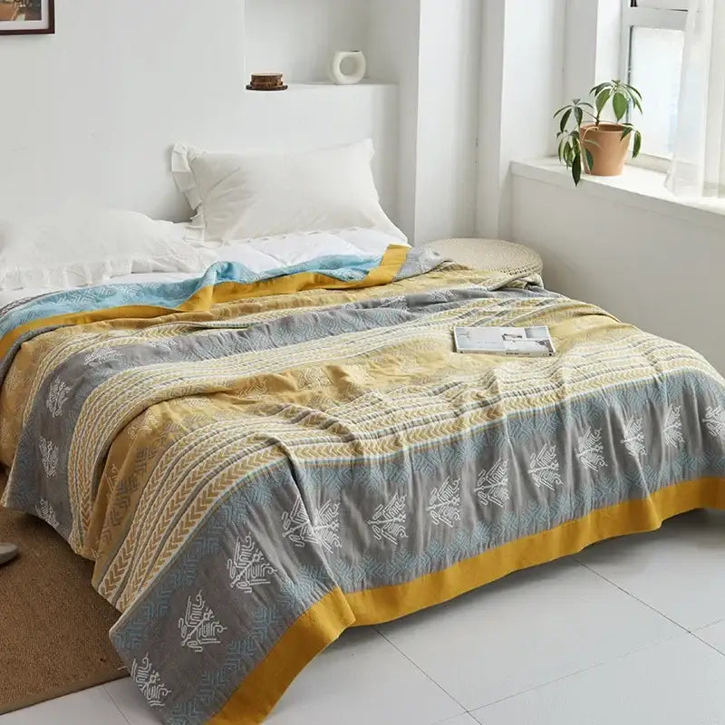 A cozy decorbites cotton gauze towel throw featuring light blue and white geometric patterns on gray and mustard stripes