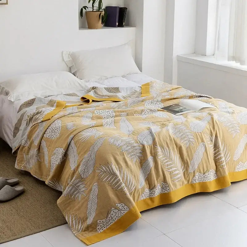 A soft mustard-yellow cotton gauze towel throw with white leaf pattern and bold yellow trim from decorbites